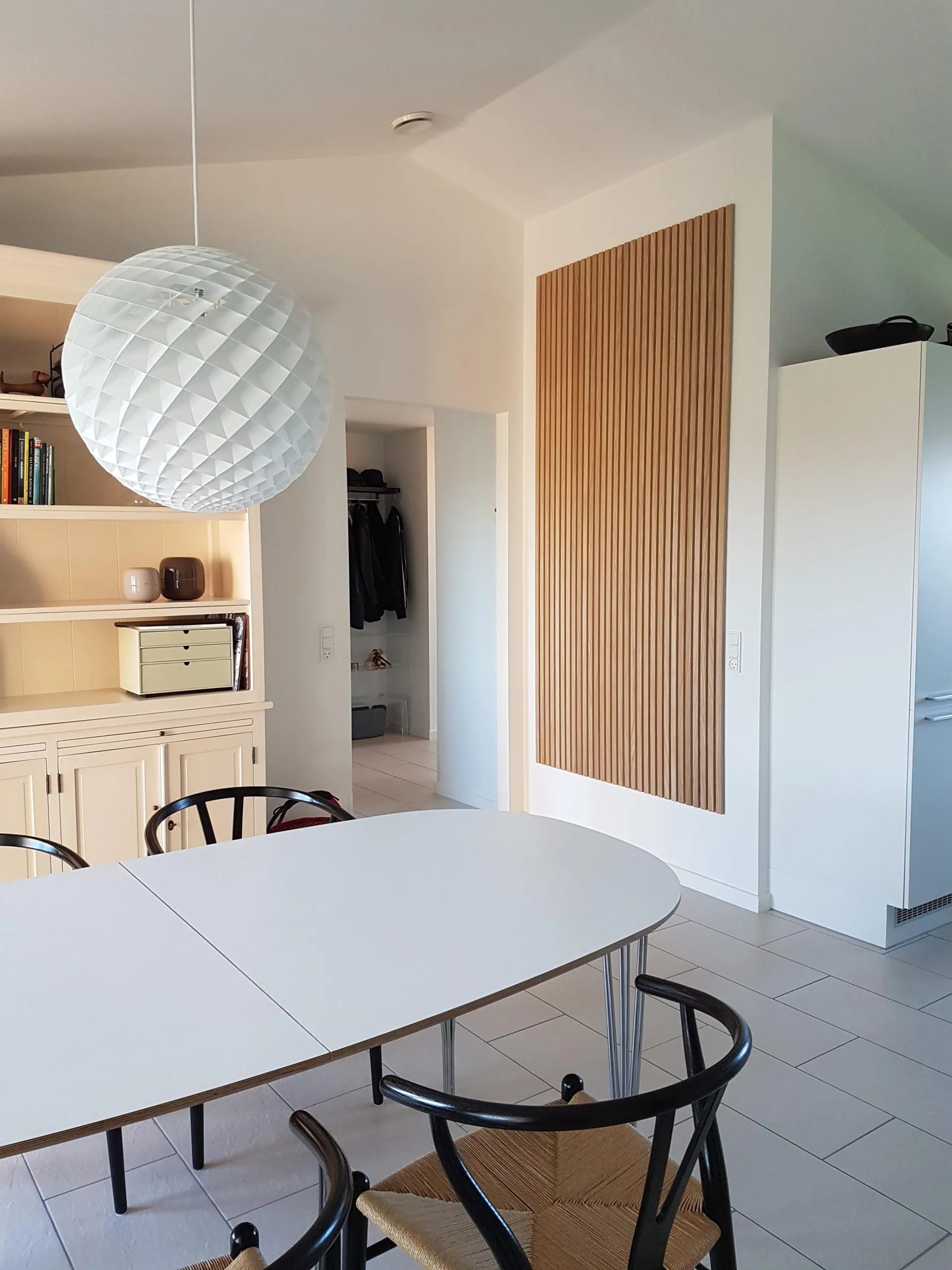 Modern dining area with a white oval table, black chairs, large textured pendant light, and sleek light wood Akupanel acoustic cabinetry.